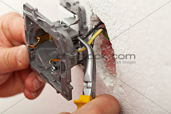 Electrician hands installing wires into electrical outlet