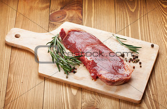 Raw sirloin steak with rosemary and spices on cutting board