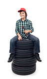 Young mechanic boy sitting on new car tires