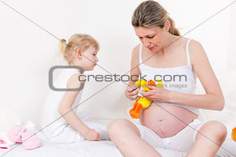 little girl and her pregnant mother with a toy for a baby