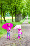 little girls wearing rubber boots with umbrellas in spring alley