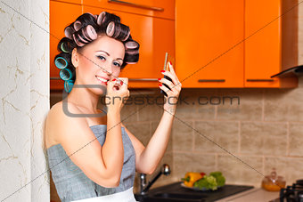 female middle-aged housewife paints her lips in the kitchen
