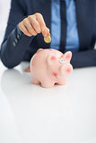 Closeup on business woman putting coin into piggy bank