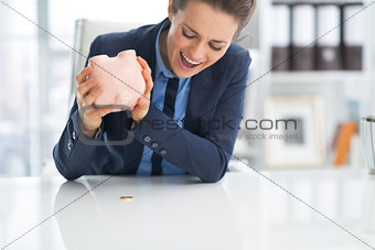 Angry business woman shaking out coin from piggy bank