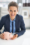 Happy business woman feeding piggy bank with coin