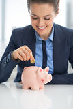 Business woman putting coin into piggy bank