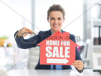 Happy realtor woman pointing on home for sale sign