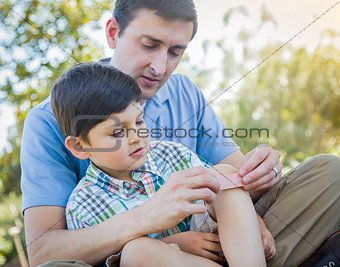 Loving Father Puts Bandage on Knee of Young Son