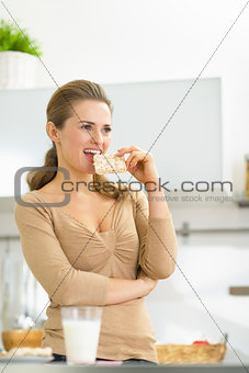 Young woman eating crisp bread in kitchen