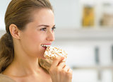 Portrait of young woman eating crisp bread in kitchen