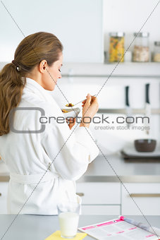 Young woman eating muesli in kitchen in the morning. rear view
