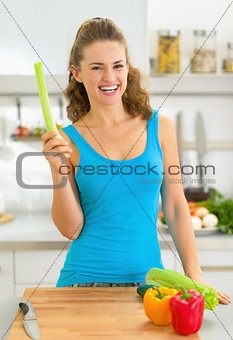 Portrait of happy young woman with fresh celery in kitchen