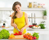Happy young woman cutting fresh vegetables in kitchen