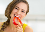 Portrait of happy young woman eating bell pepper in kitchen