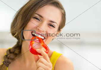 Portrait of happy young woman eating bell pepper in kitchen