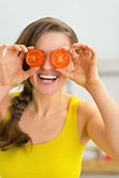 Happy young woman holding tomato slices in front of eyes
