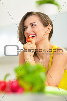 Young woman eating tomato in kitchen