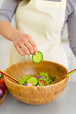 Closeup on young woman adding cucumber in salad