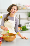 Happy young woman making salad in kitchen