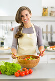 Happy young housewife making salad in kitchen