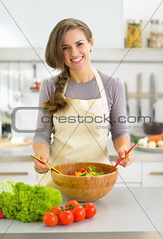 Happy young housewife making salad in kitchen