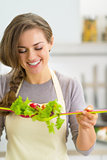 Portrait of happy young housewife making salad in kitchen