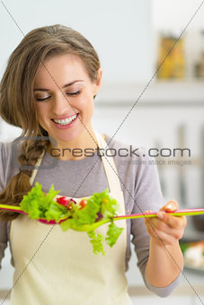 Portrait of happy young housewife making salad in kitchen