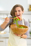 Portrait of happy young housewife tasting salad in kitchen