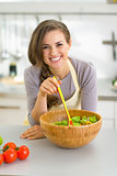 Portrait of happy young housewife with salad in kitchen