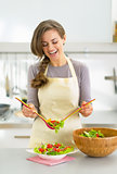 Happy young housewife serving salad in kitchen