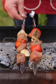 meat roasted on the fire skewers (shashlik) with tomatoes and mushrooms man in the background
