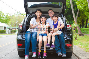 happy family sitting in the car and their house behind