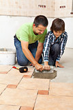 Boy learning how to spread adhesive for ceramic floor tiles