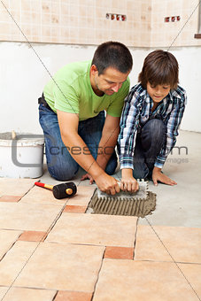 Boy learning how to spread adhesive for ceramic floor tiles