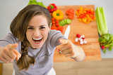 Happy young housewife in kitchen pointing in camera