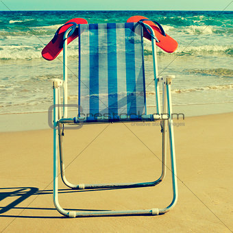 deckchair and orange flip-flops on the beach, with a retro effec