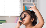 Indian girl peeking through magnifying glass.