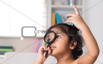 Indian girl peeking through magnifying glass.