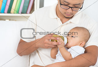 Father bottle feeding baby at home.