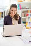 Smiling fashion designer working on laptop in office