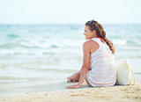 Young woman sitting on beach in the evening and looking into dis