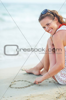Happy young woman sitting on beach and drawing on sand
