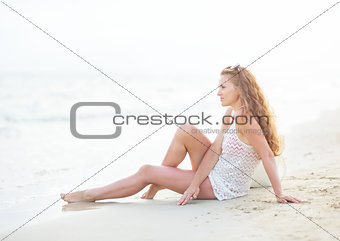 Happy young woman sitting on beach in the evening