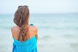 Young woman in towel on beach looking into distance. rear view