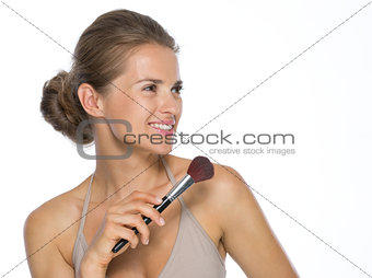 Young woman with makeup brush looking on copy space