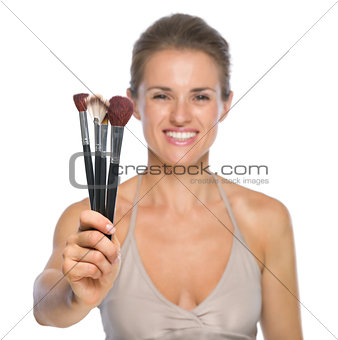 Closeup on smiling young woman showing makeup brushes