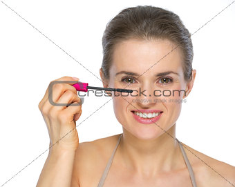 Happy young woman applying mascara