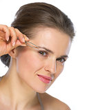Young woman using tweezers on brow