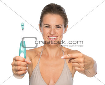 Portrait of smiling young woman pointing on toothbrushâ