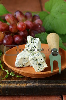 pieces of blue cheese with red grapes on a wooden table